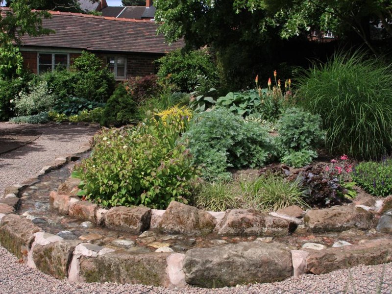 Curved man-made stream of senses garden with ornamental and fragrant bedding in curve, building in background